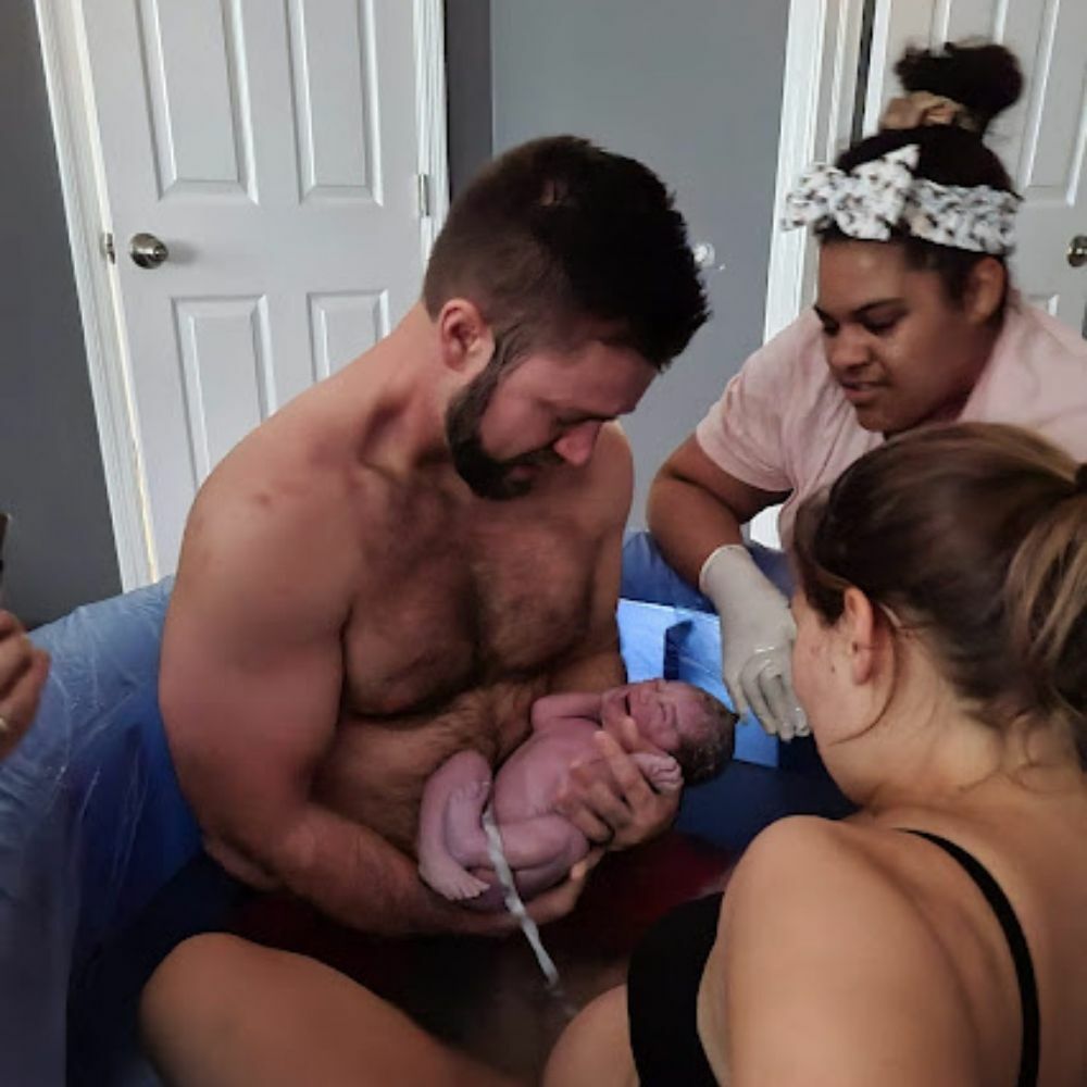 man holding newborn baby in birthtub